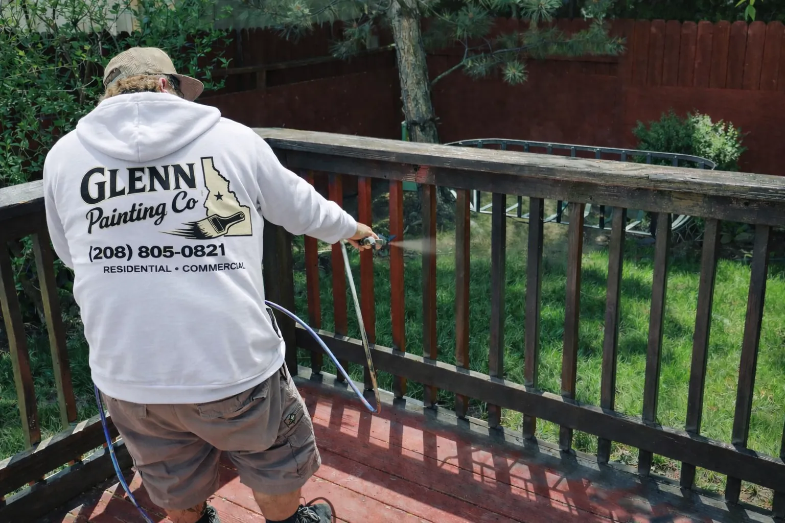 Glenn Painting Co painter in branded hoodie staining a backyard deck and railing in Star, Idaho