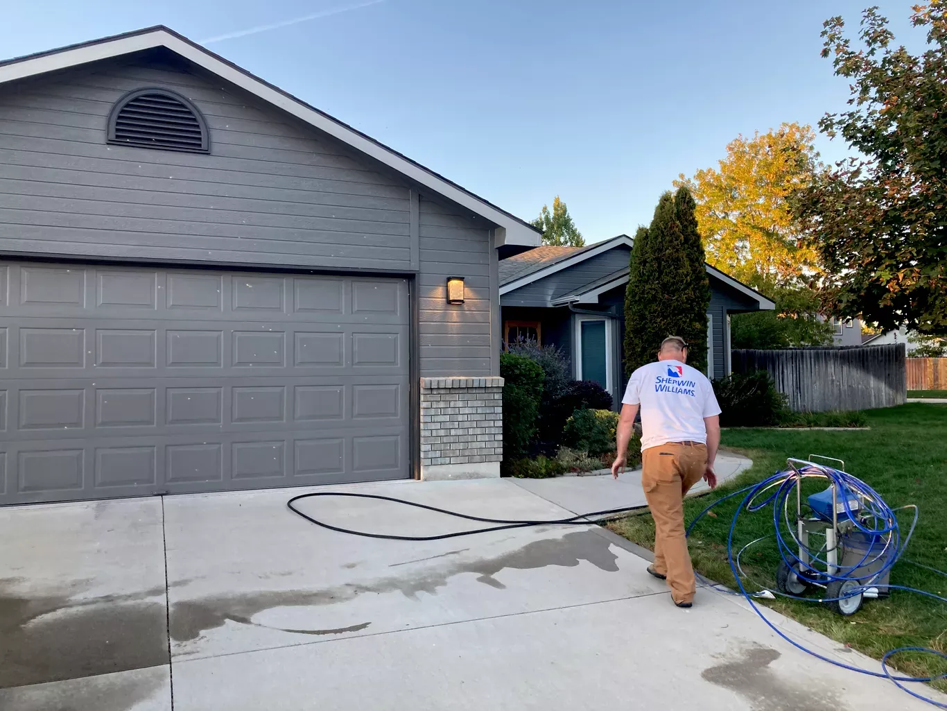 Painter spraying a gray home exterior and garage with an airless sprayer in Star, Idaho