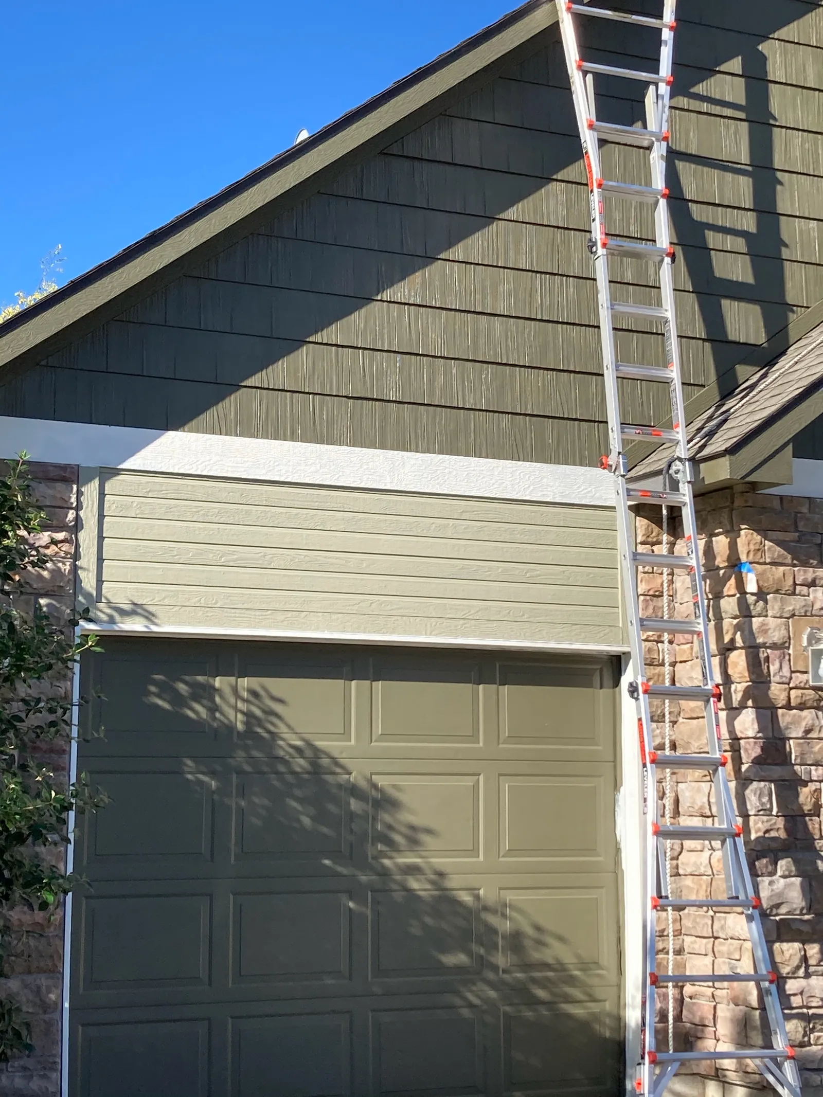 Green lap siding and garage door being repainted from a ladder on a Star, Idaho home