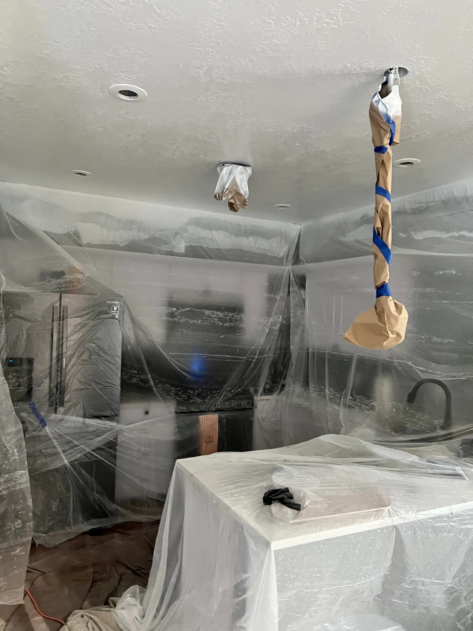 Kitchen fridge, island and cabinets wrapped in plastic before interior spraying